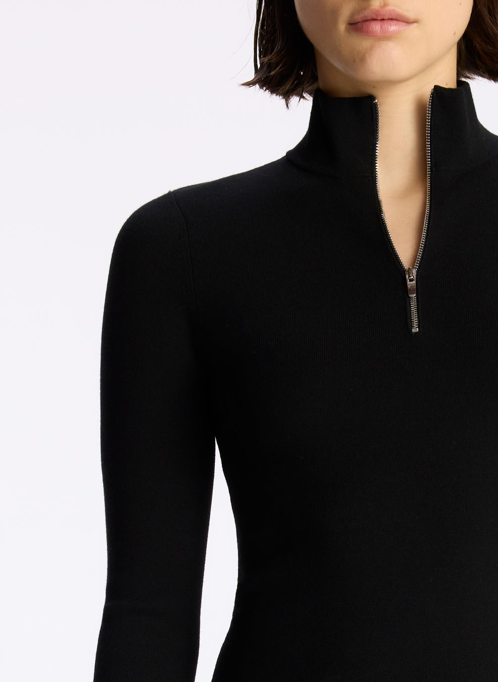 detail view of woman wearing black half zip compact knit long sleeve top and black pants