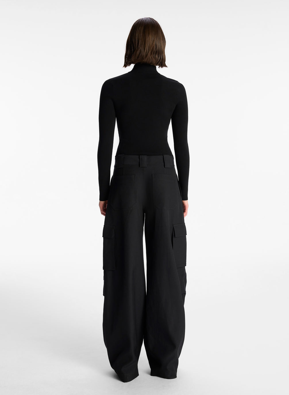 back view of woman wearing black half zip compact knit long sleeve top and black pants