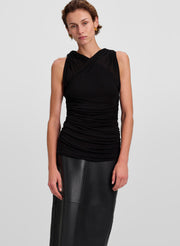 A model wearing a black sleeveless ruched top with a crossover neckline and a black leather-look skirt, photographed against a light gray studio background.