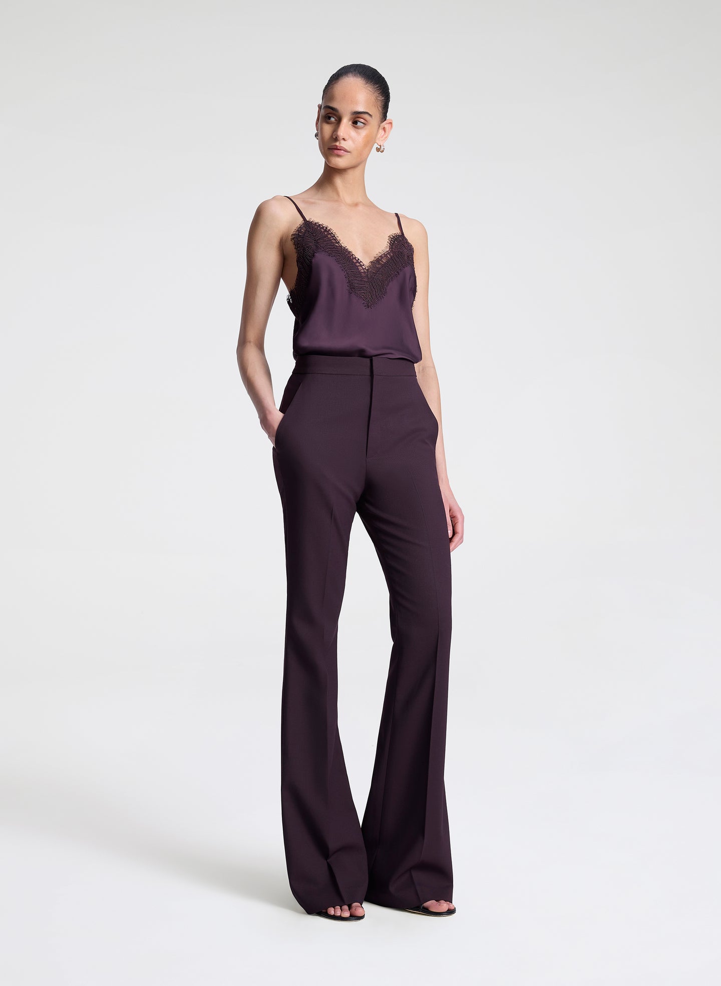 Woman wearing a dark purple lace-trimmed top and pants on a light gray background