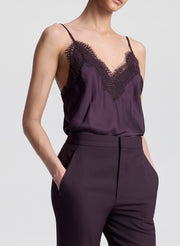 Woman wearing a dark purple lace-trimmed top and pants on a light gray background