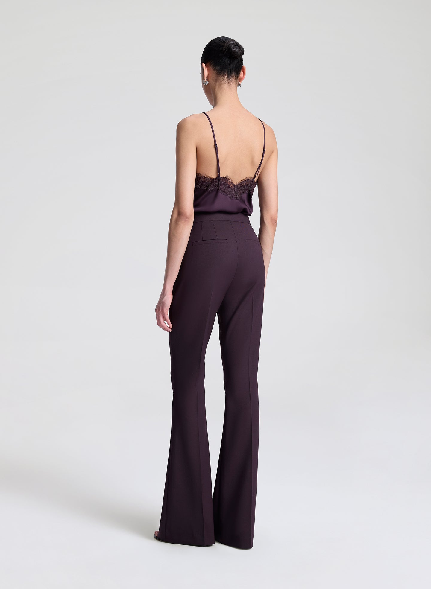 Woman wearing a dark purple lace-trimmed top and pants on a light gray background