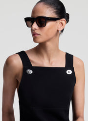 Woman wearing a black sleeveless mini dress with button details against a light gray background