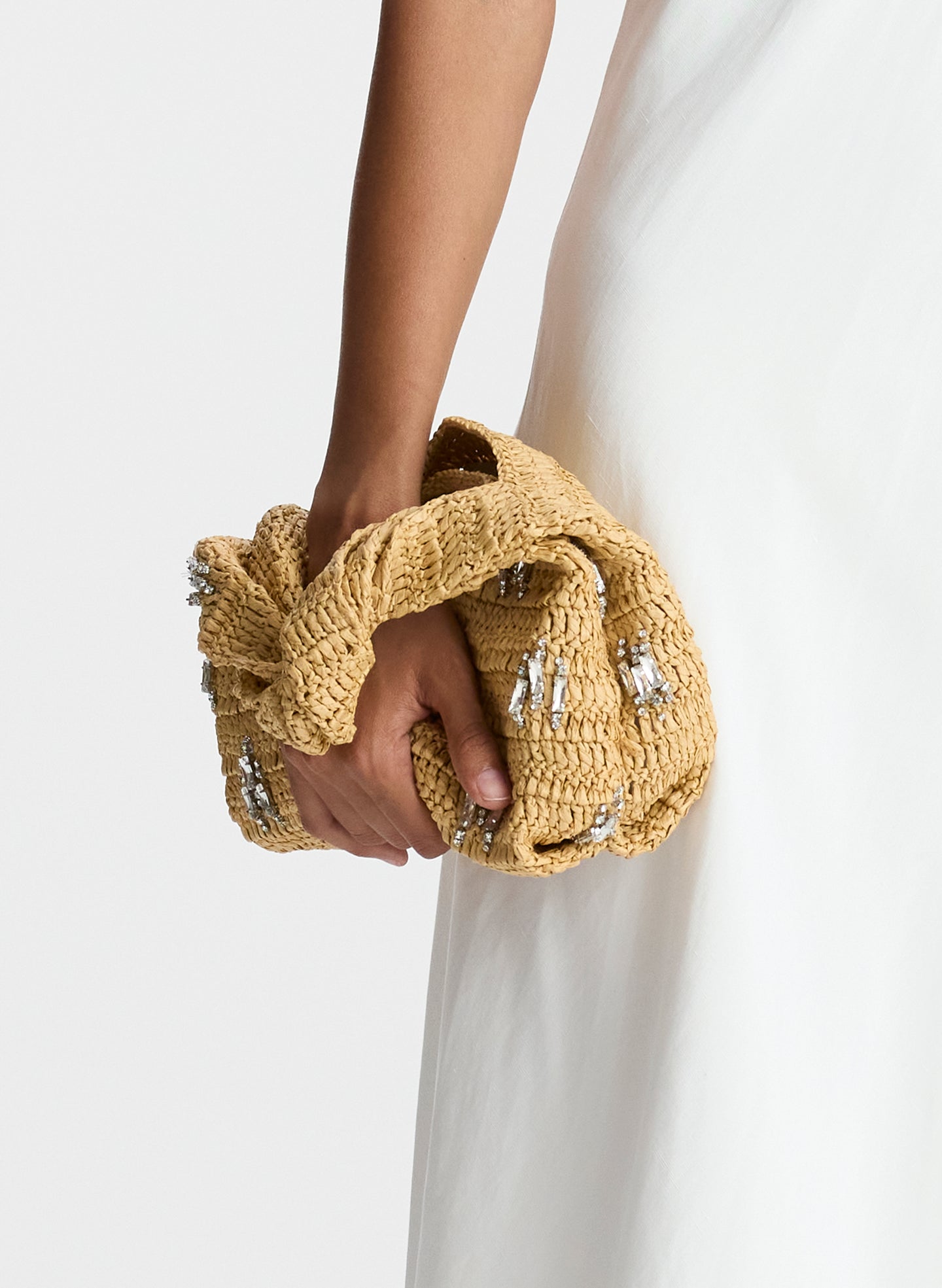 flat lay view of light tan raffia short length top handle bag with small sized rectangular base and rhinestone embellishments