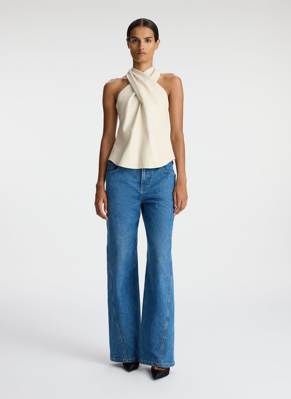 front view of woman wearing cream vegan leather halter top and medium blue wash denim jeans