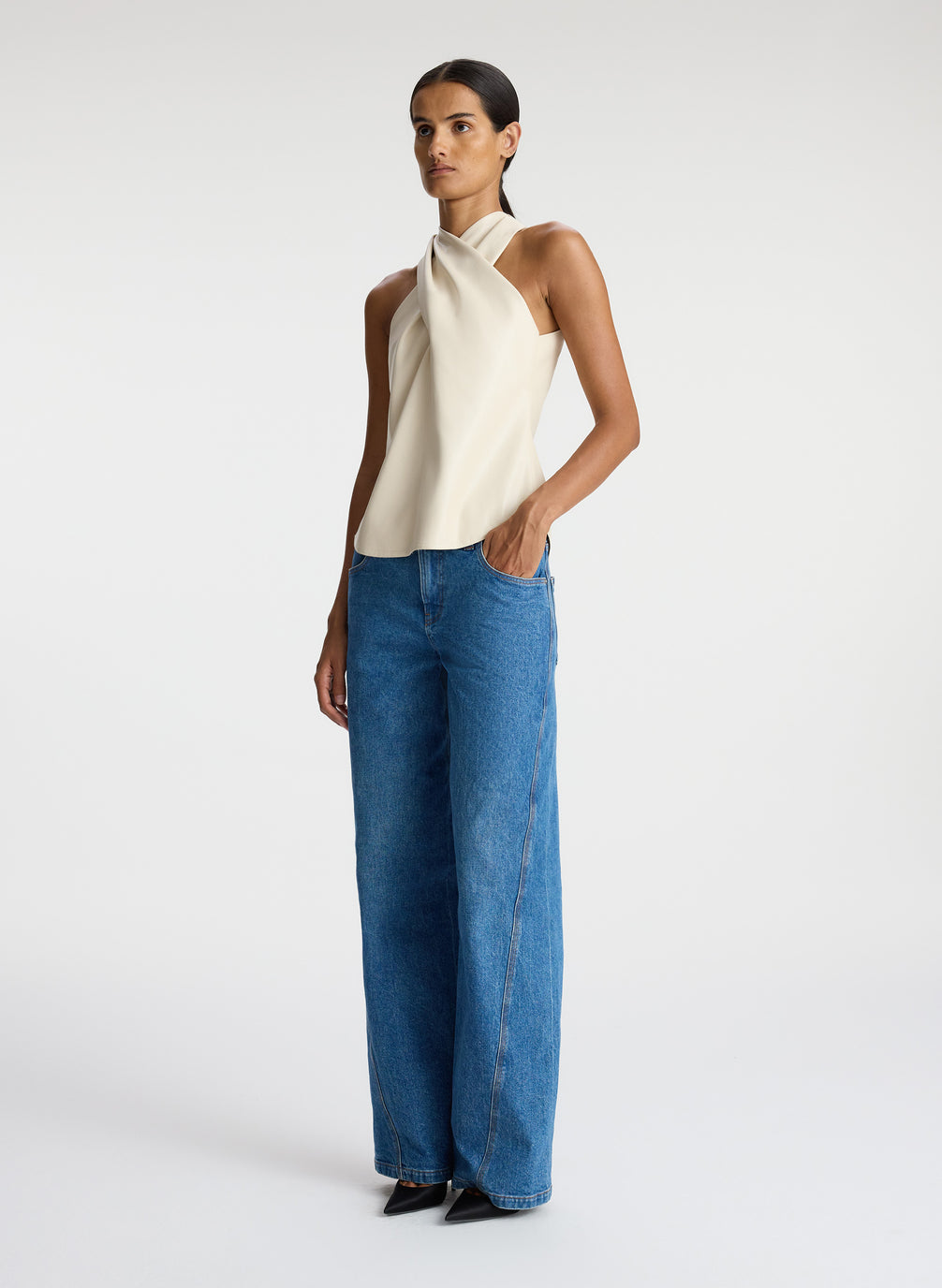 side view of woman wearing cream vegan leather halter top and medium blue wash denim jeans