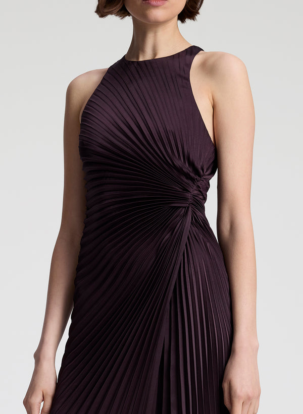 Woman wearing a dark purple pleated dress on a light gray background