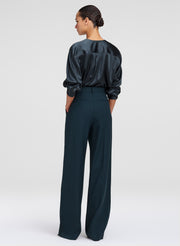 A woman shown from the back wearing a dark satin long-sleeve top and matching dark wide-leg trousers against a light gray studio background.