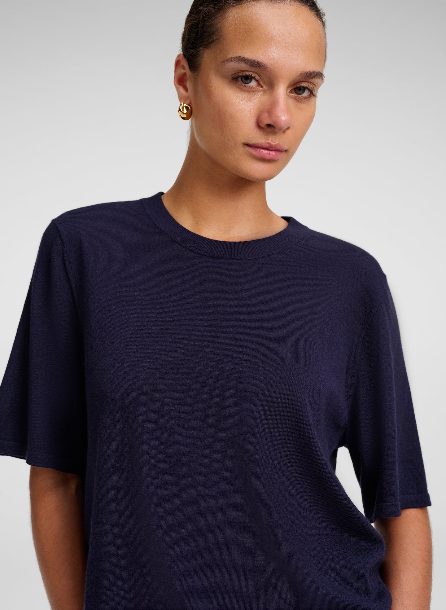 A woman wearing a dark navy blue short-sleeve crewneck t-shirt, photographed against a neutral light gray studio background.