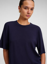 A woman wearing a dark navy blue short-sleeve crewneck t-shirt, photographed against a neutral light gray studio background.