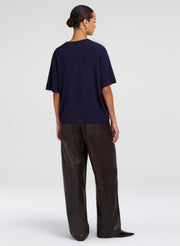 A model shown from the back wearing an oversized navy blue short-sleeve t-shirt and dark brown wide-leg trousers, photographed against a light gray studio background.