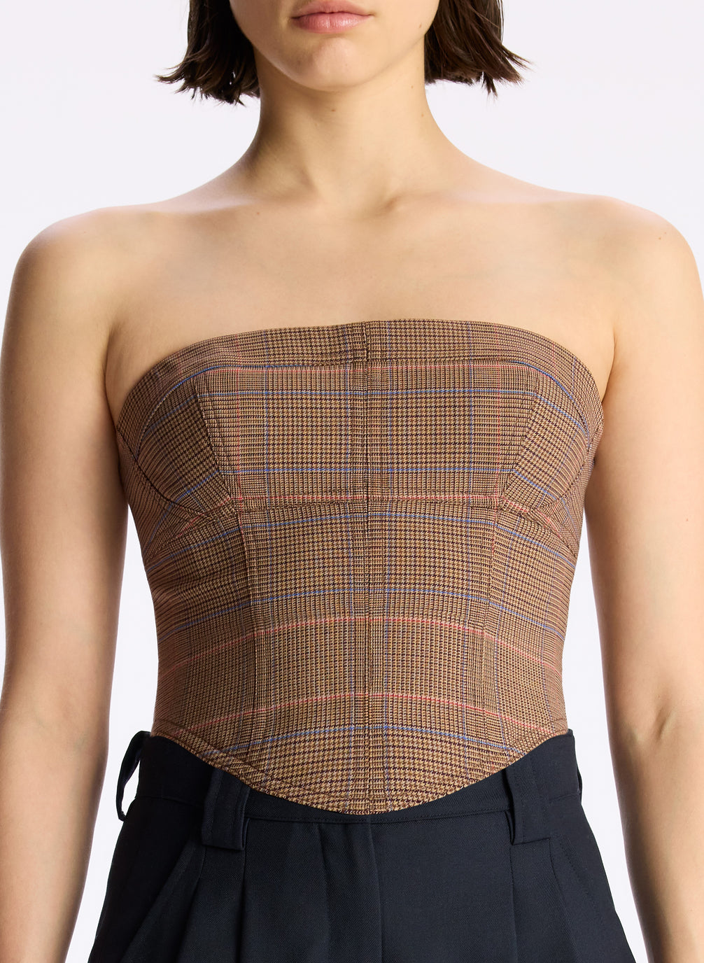 detail view of woman wearing brown plaid strapless top and black pants