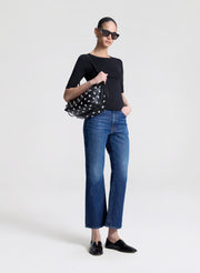 Woman wearing a black top and blue jeans, holding a studded handbag on a white background