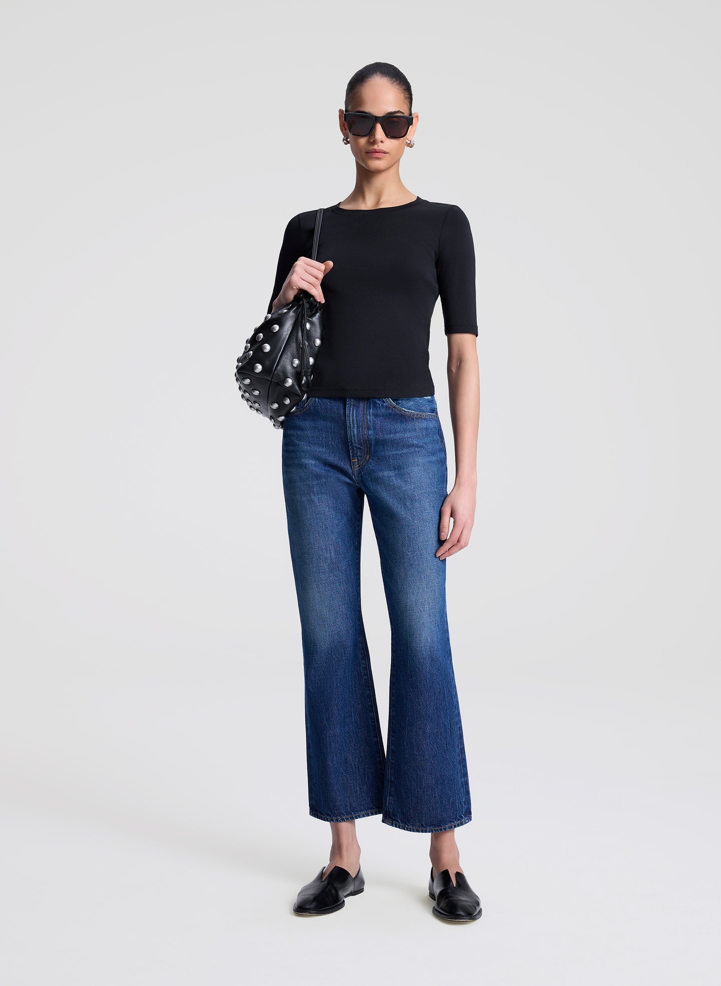 Woman wearing a black top and blue jeans holding a polka dot handbag on a white background