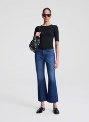 Woman wearing a black top and blue jeans holding a polka dot handbag on a white background