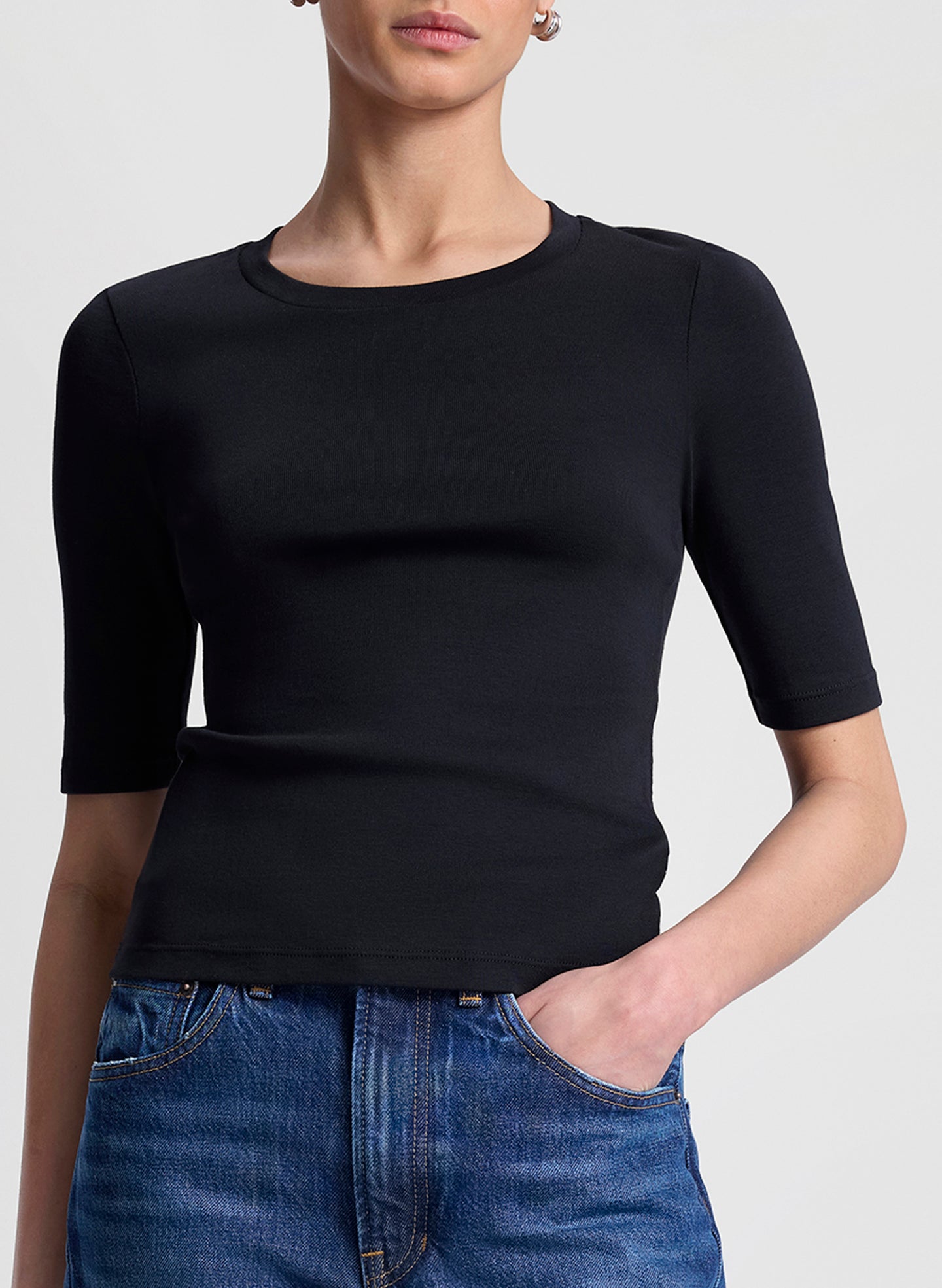 Person wearing a black short-sleeve top and blue jeans on a light gray background