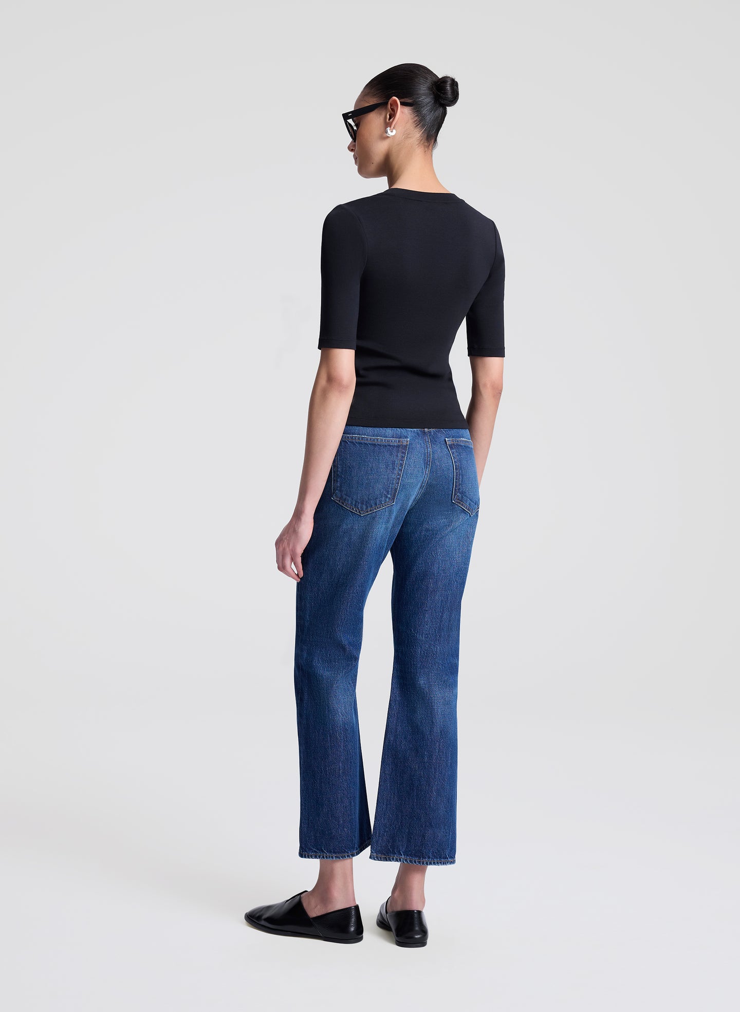 Woman wearing a black top and blue jeans on a white background