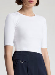 Person wearing a white short-sleeve top and dark pants on a light gray background