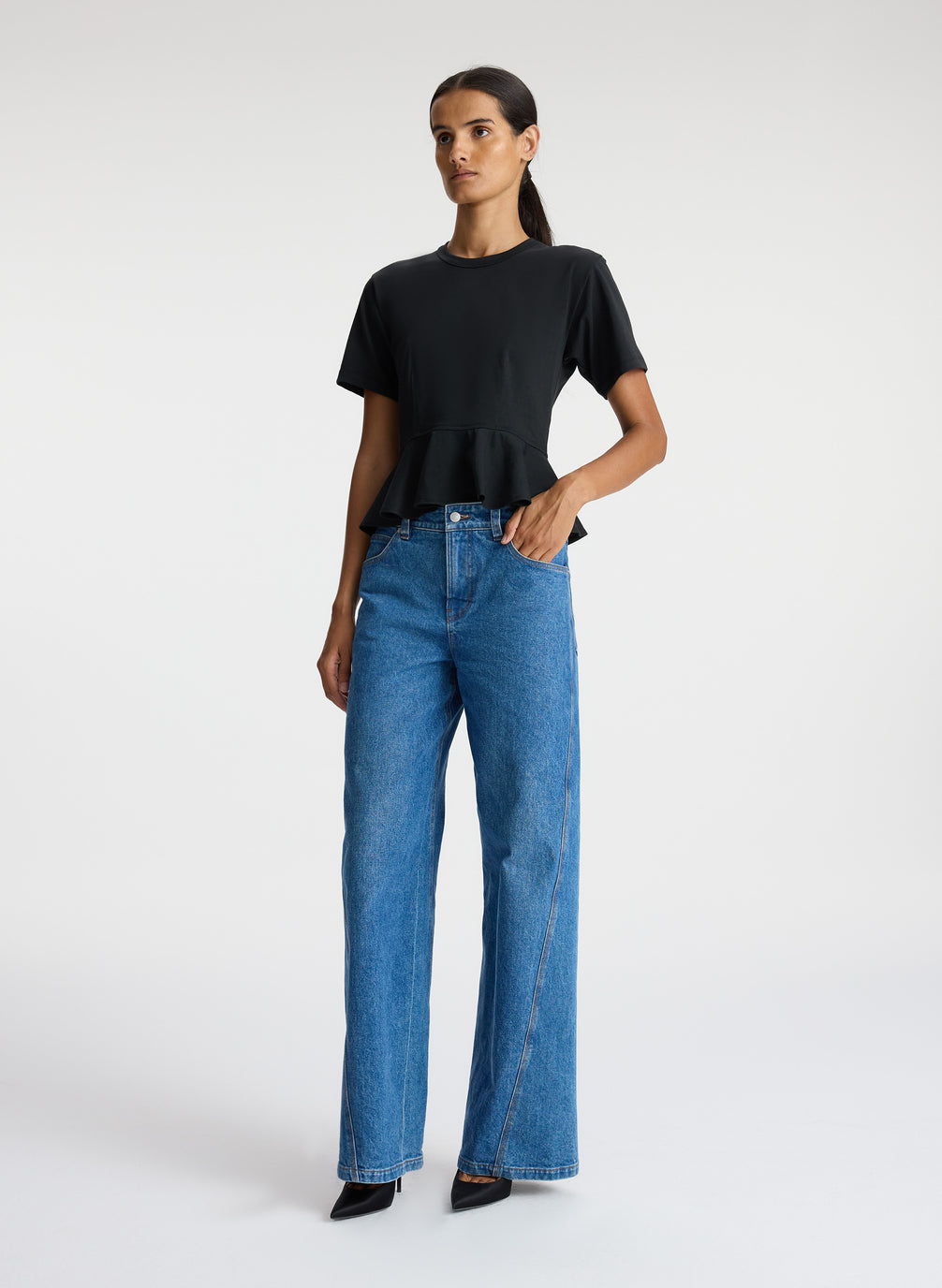 side view of woman wearing black peplum tee and blue jeans