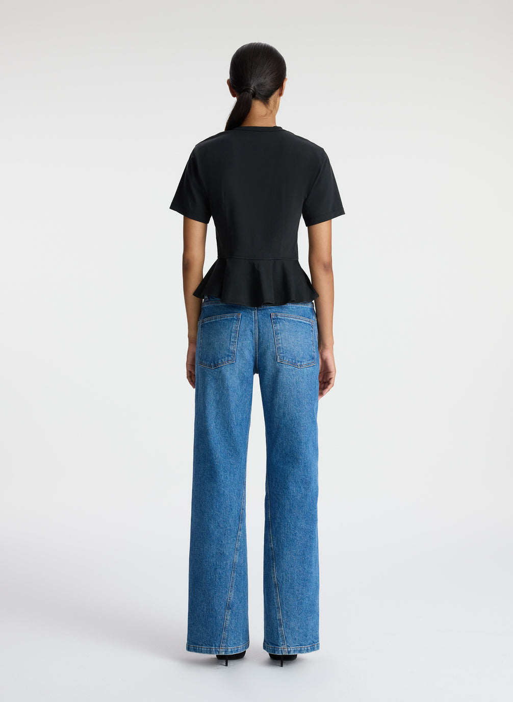 back view of woman wearing black peplum tee and blue jeans