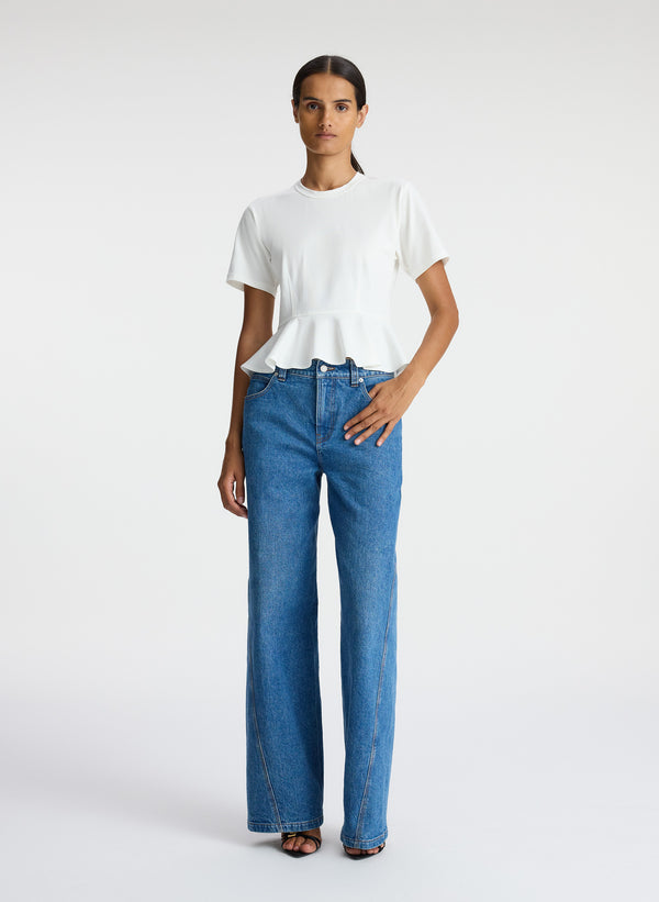 front view of woman wearing white peplum tee and medium blue jeans