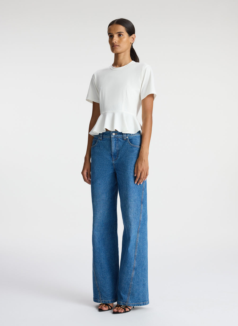 side  view of woman wearing white peplum tee and medium blue jeans