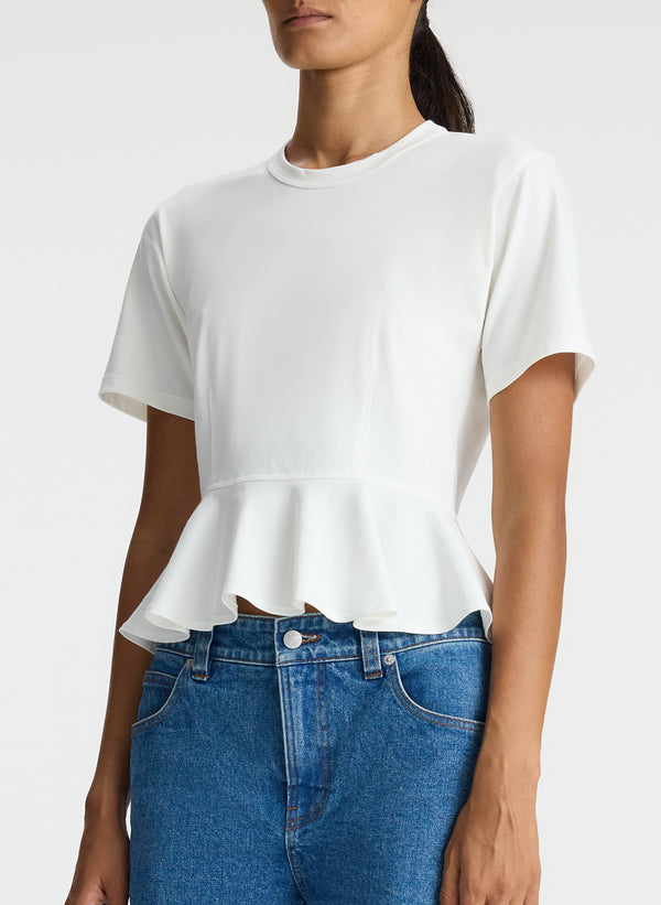 detail  view of woman wearing white peplum tee and medium blue jeans