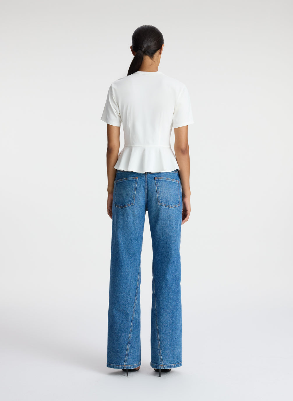 back  view of woman wearing white peplum tee and medium blue jeans