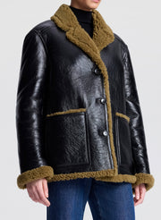 Person wearing a black leather jacket with brown shearling on a white background