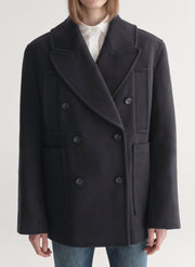 Person wearing a navy blue coat over a white shirt and blue jeans 