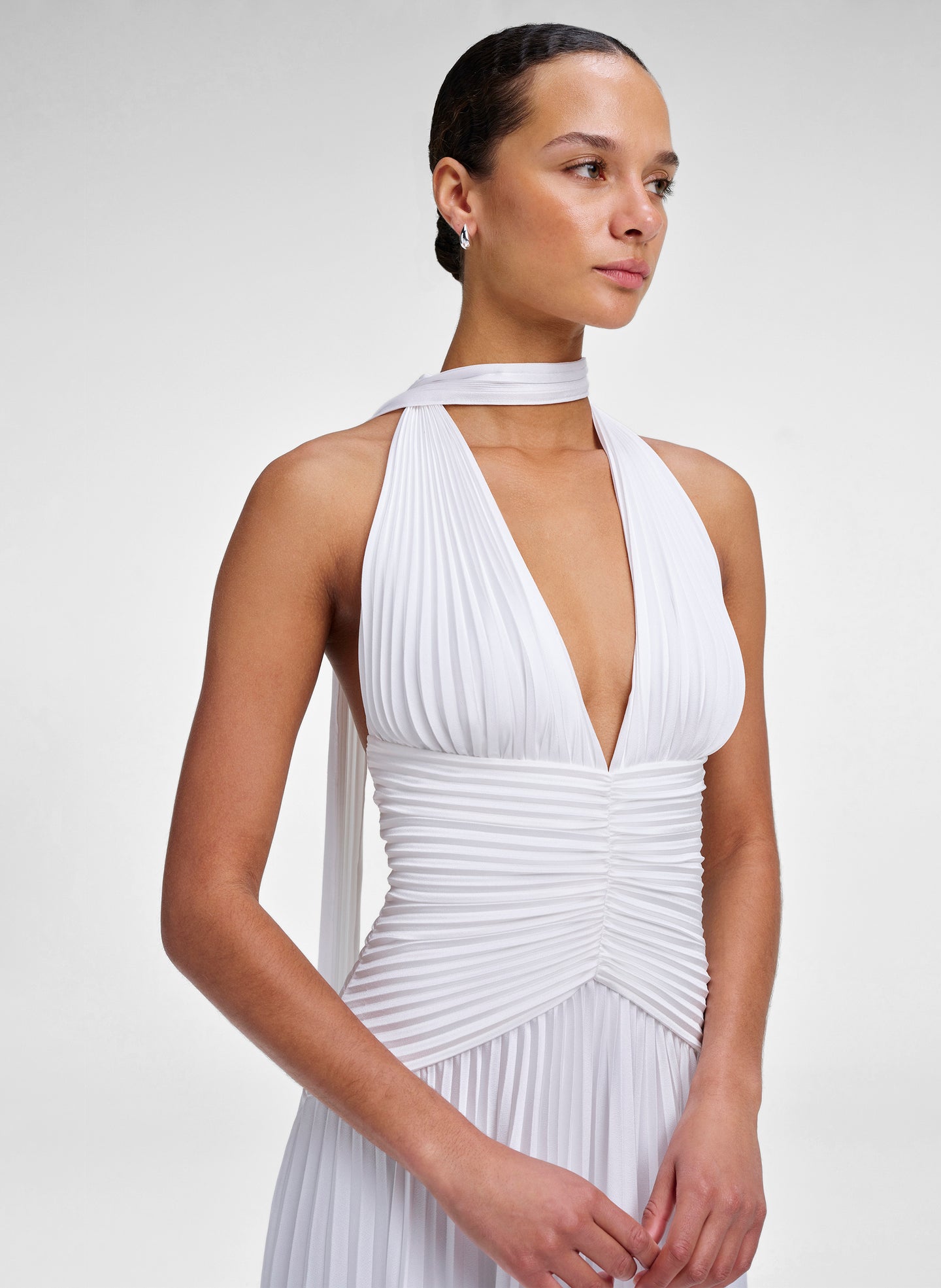Woman wearing a white pleated dress against a plain background
