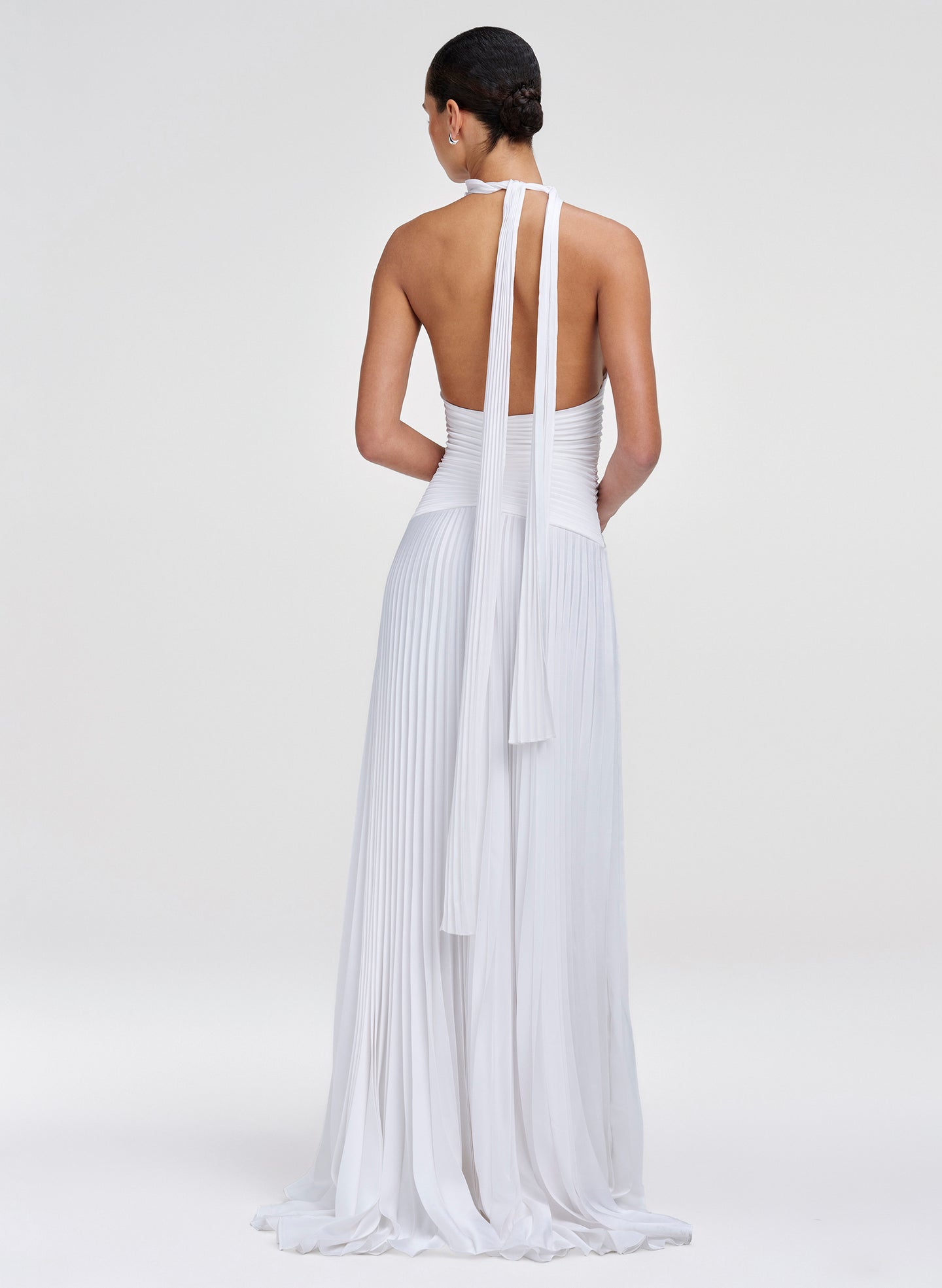 Woman wearing a white halter neck dress with pleated skirt on a light gray background