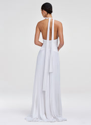 Woman wearing a white halter neck dress with pleated skirt on a light gray background