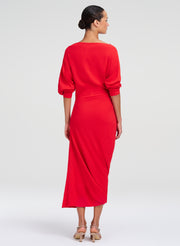 A woman modeling a bright red midi dress from the back, featuring three-quarter balloon sleeves and a gathered waist, set against a plain light gray studio background.