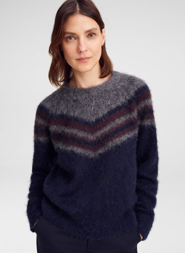 A woman wearing a fuzzy knit crewneck sweater with a chevron pattern in navy blue, dark gray, and burgundy, photographed against a light gray studio background.