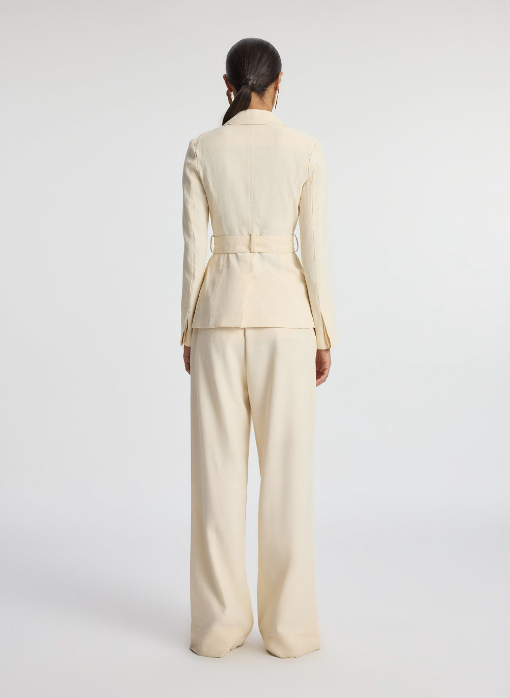 back view of woman wearing beige belted jacket and beige wide leg pants