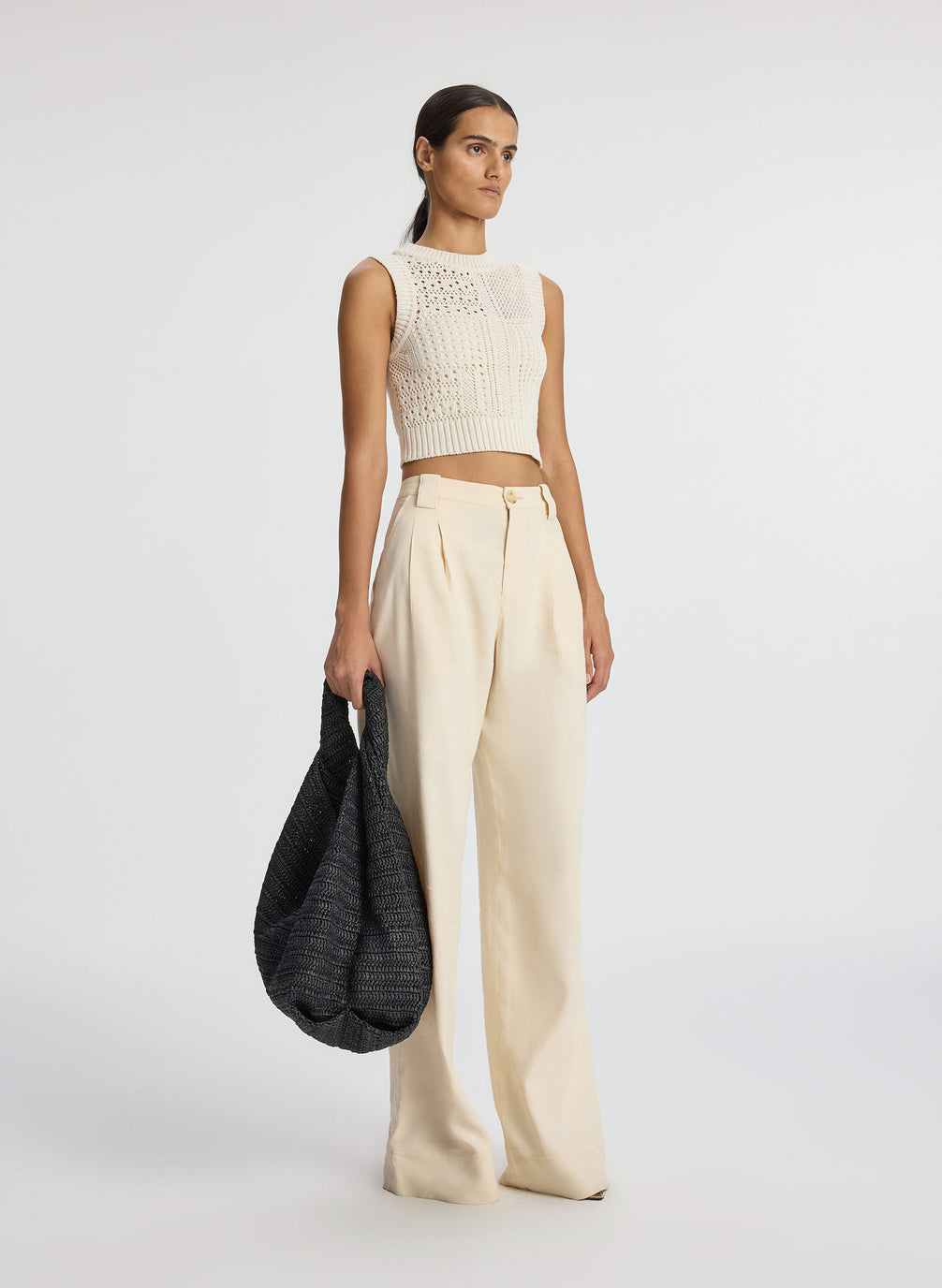 side view of woman wearing cream sleeveless cropped crochet top and beige pants