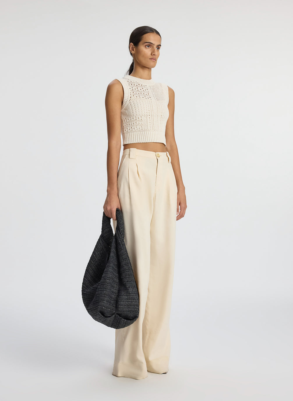 side view of woman wearing cream sleeveless cropped crochet top and beige pants