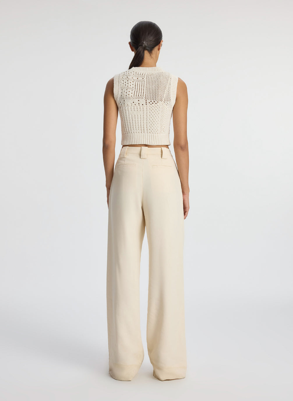 back view of woman wearing cream sleeveless cropped crochet top and beige pants