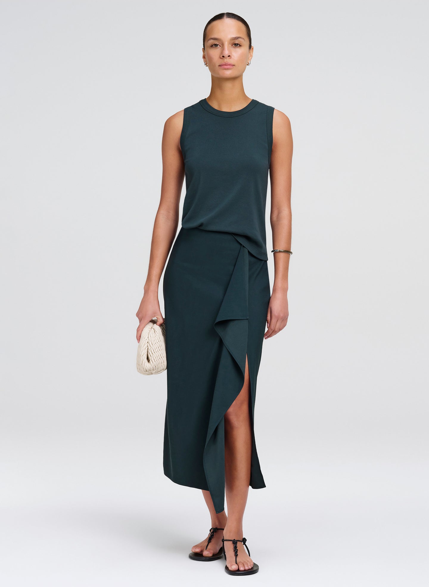 Woman wearing a dark green sleeveless top with matching skirt with a slit on a white background