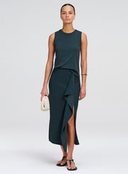 Woman wearing a dark green sleeveless top with matching skirt with a slit on a white background