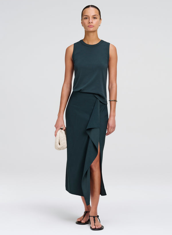 Woman wearing a dark green sleeveless top with matching skirt with a slit on a white background