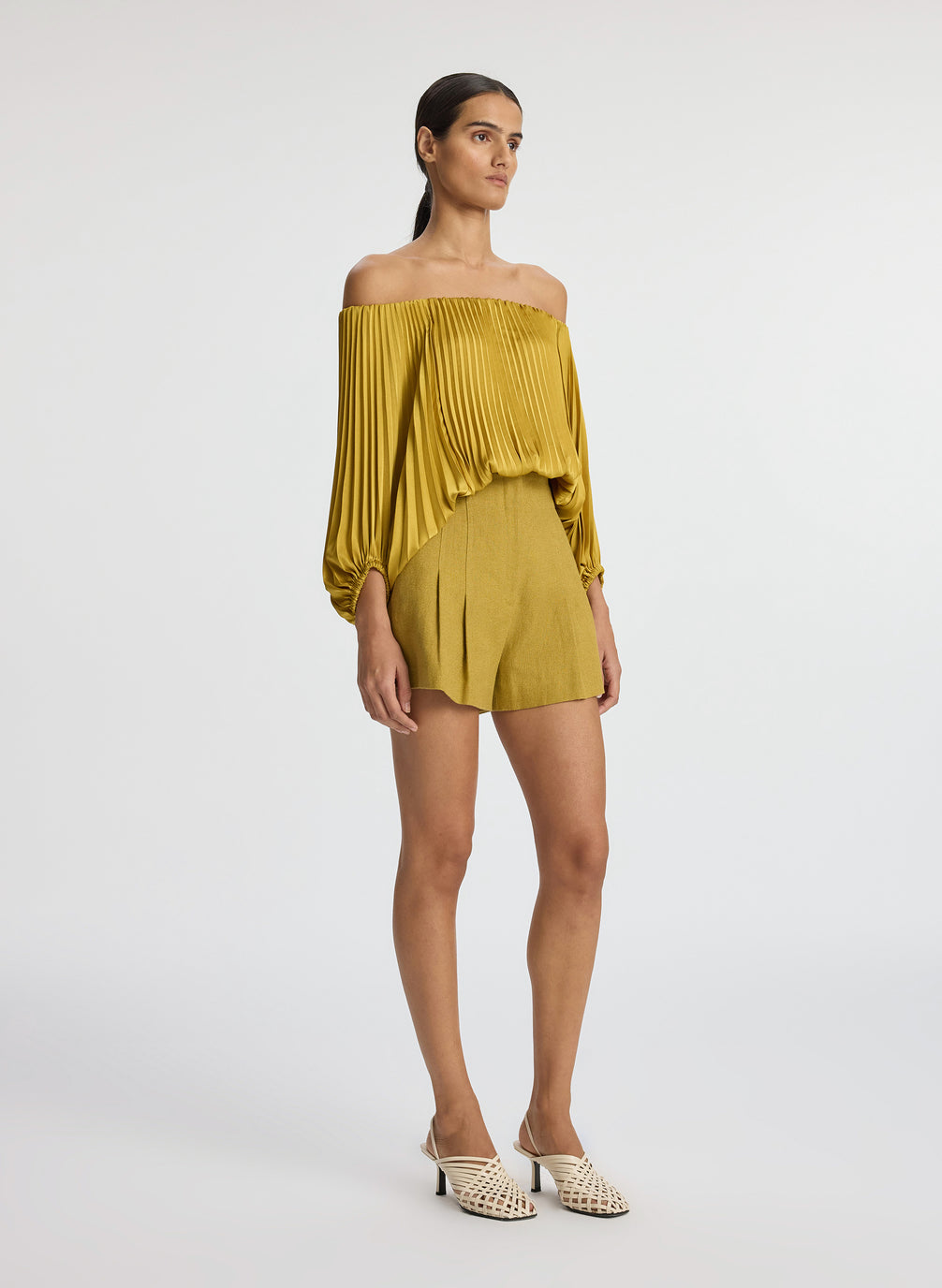 side view of woman wearing yellow pleated off shoulder top and yellow shorts