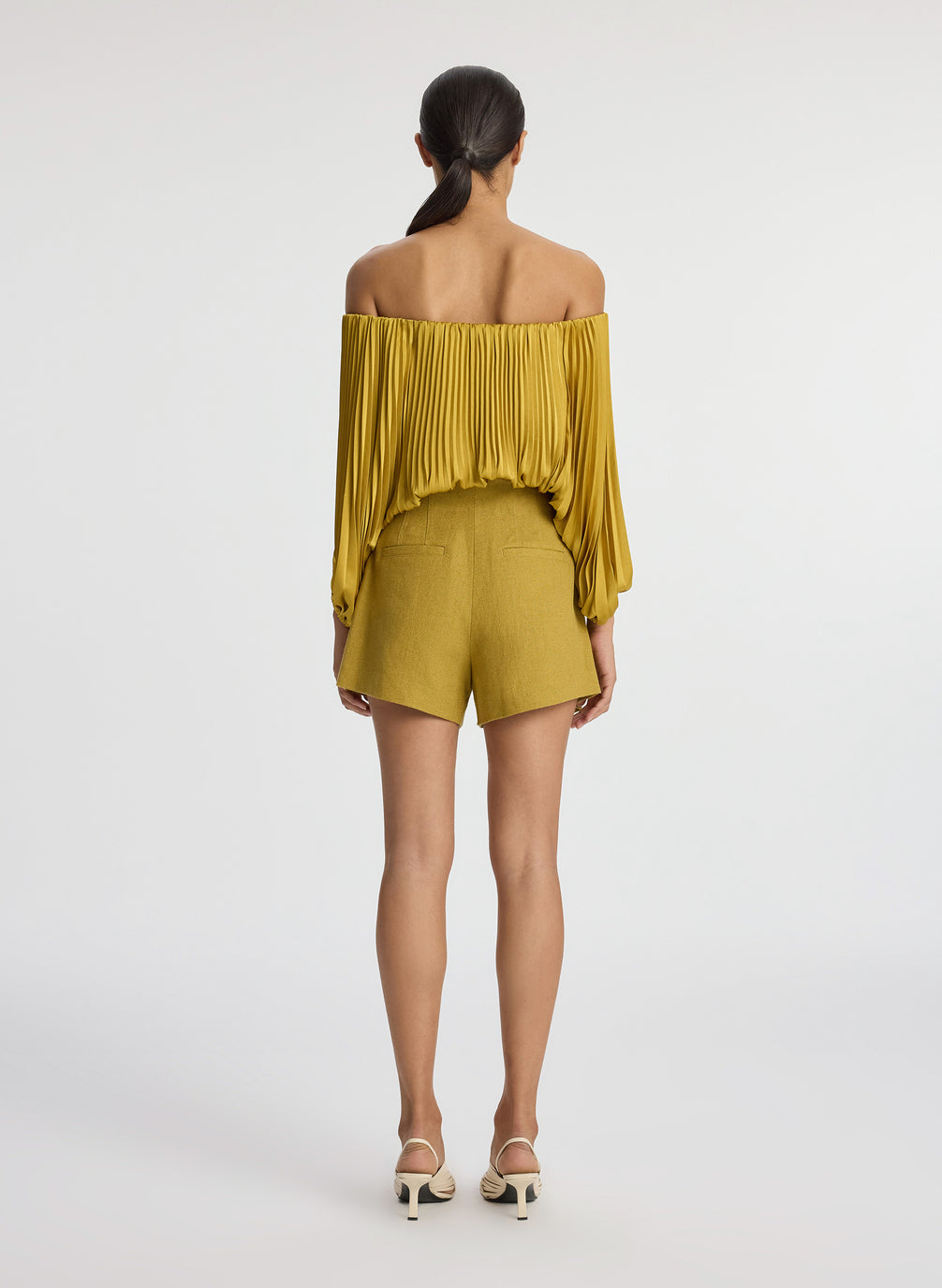 back view of woman wearing yellow pleated off shoulder top and yellow shorts