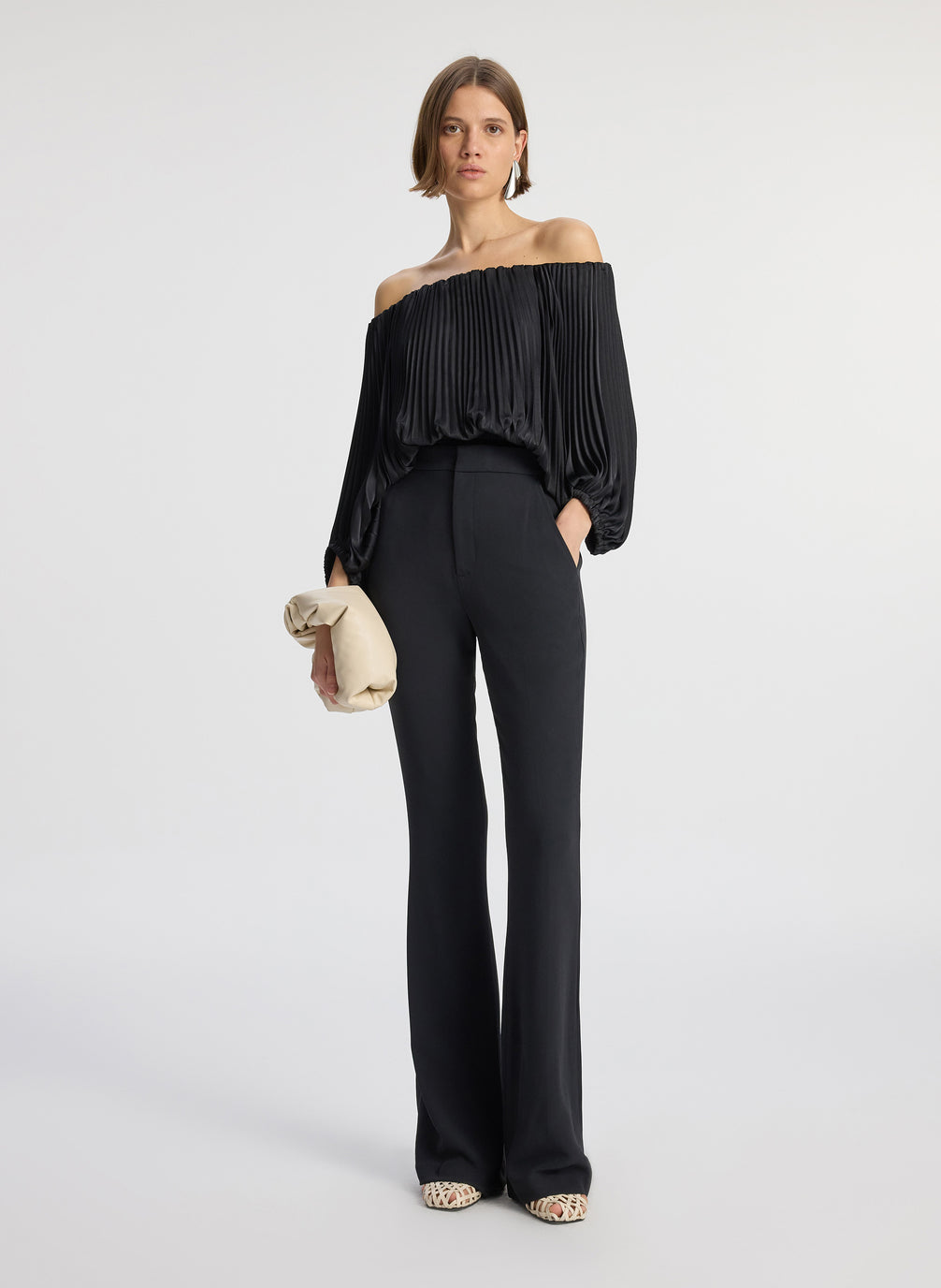 front view of woman wearing black satin pleated off the shoulder top with black pants