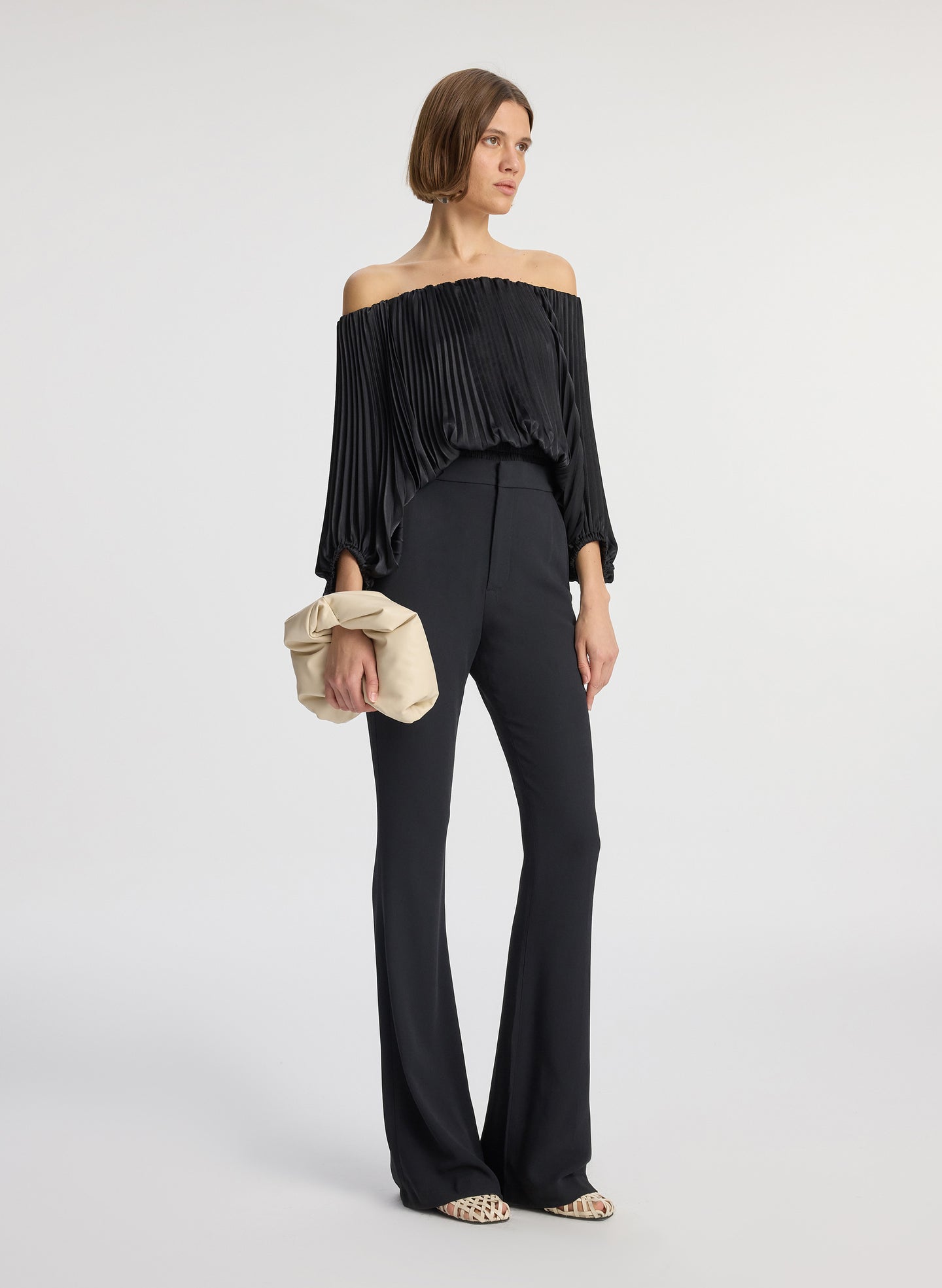 side view of woman wearing black satin pleated off the shoulder top with black pants