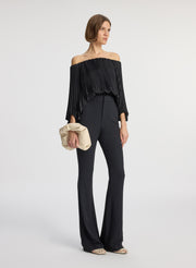 side view of woman wearing black satin pleated off the shoulder top with black pants