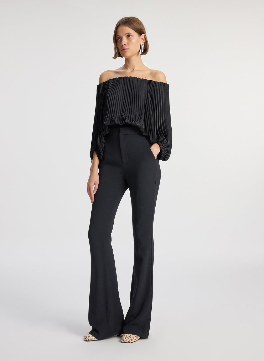 side view of woman wearing black satin pleated off the shoulder top with black pants