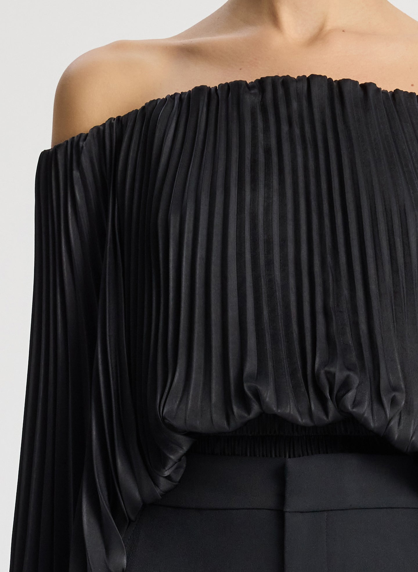 detail view of woman wearing black satin pleated off the shoulder top with black pants