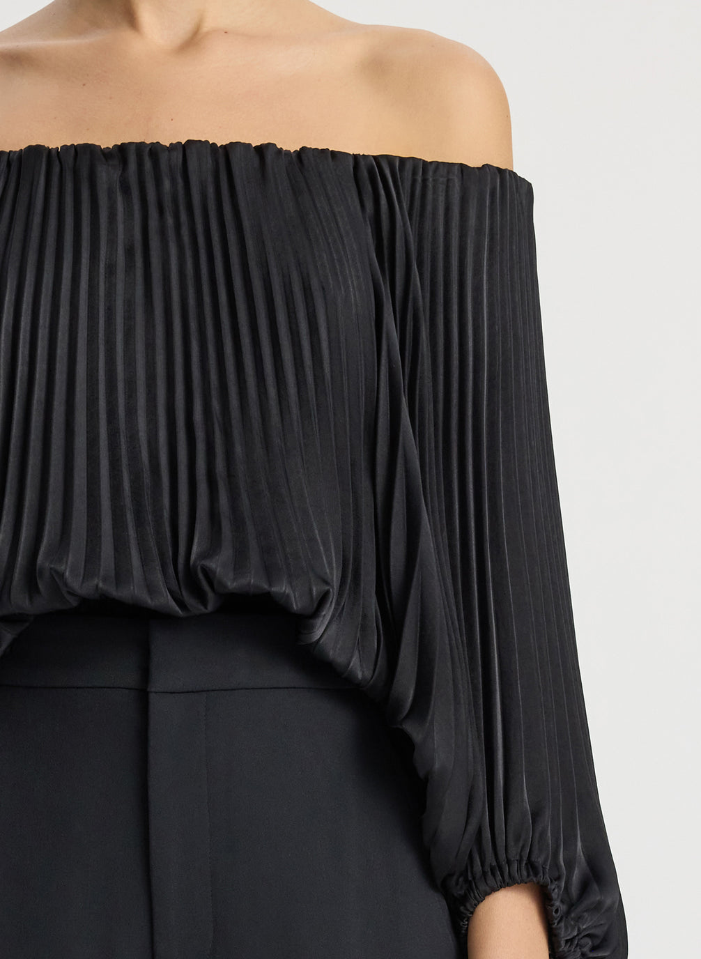 detail view of woman wearing black satin pleated off the shoulder top with black pants
